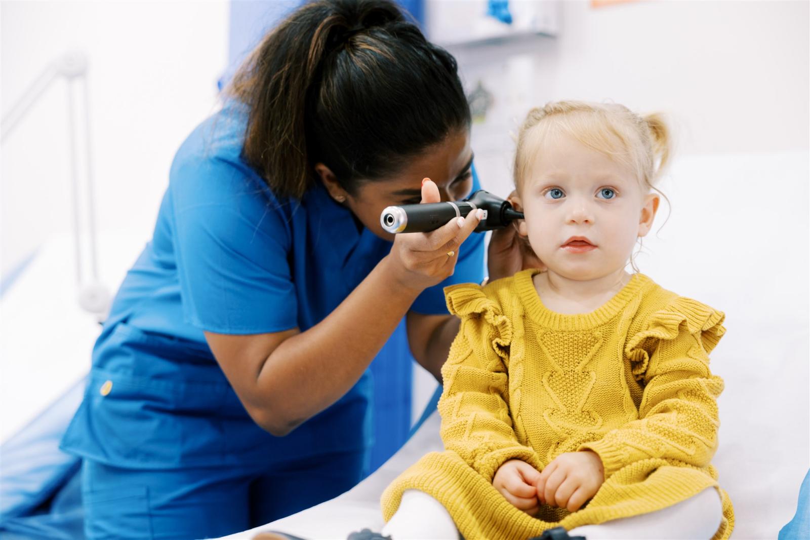 Healthcare professional examining toddler's ear with otoscope during child health assessment