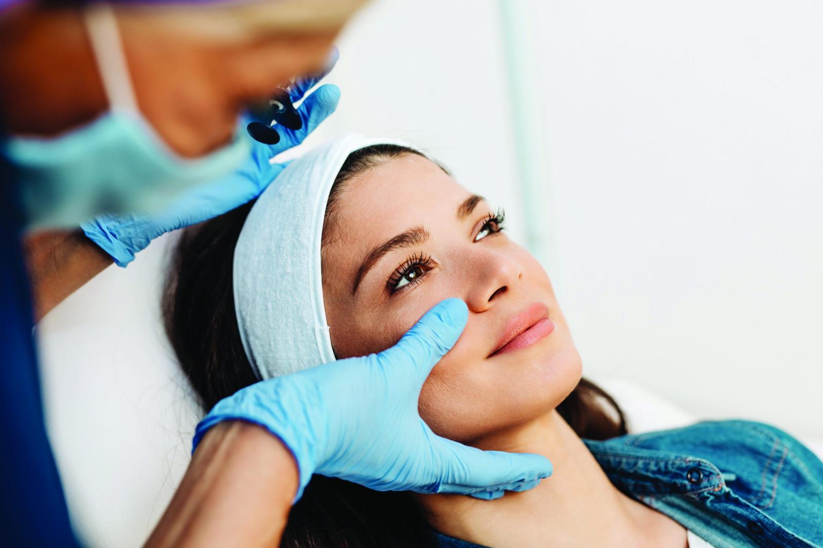 Healthcare professional performing medical skin assessment on patient's face wearing protective gloves