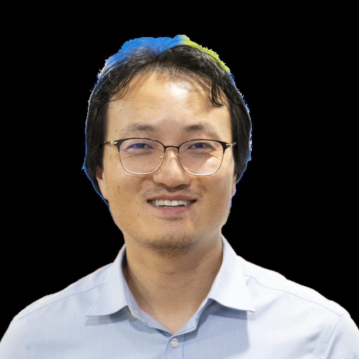 Professional headshot of smiling Asian male doctor wearing glasses and light blue shirt against white background