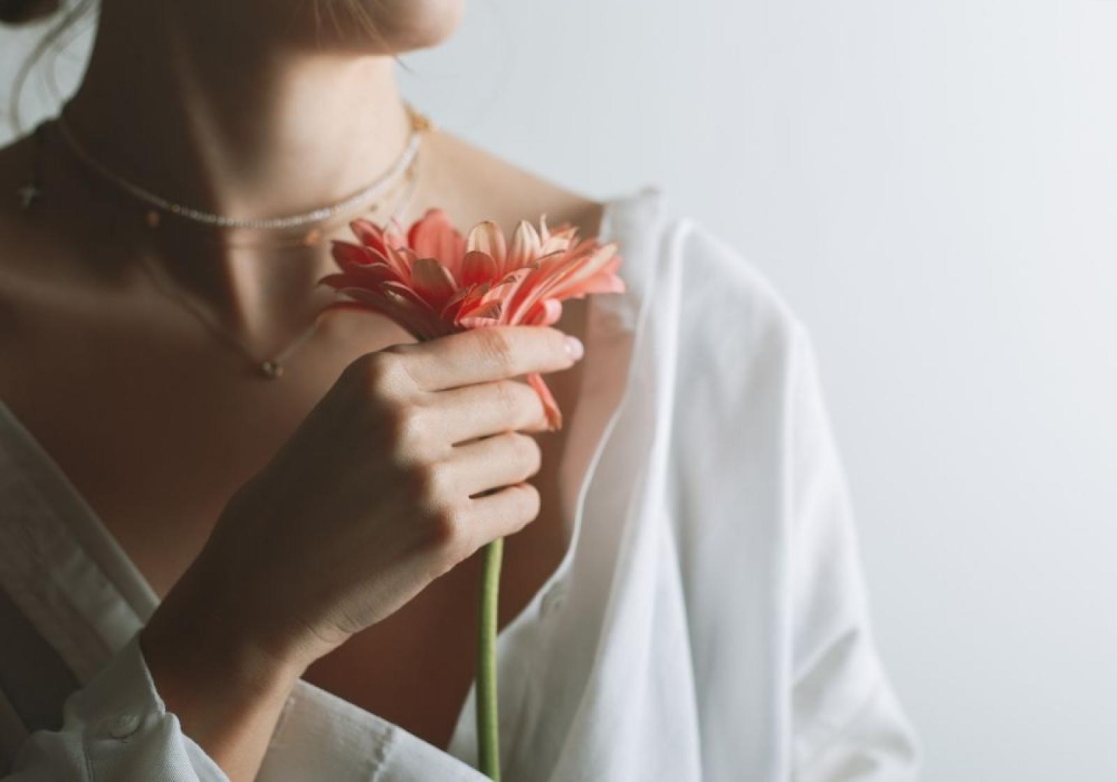 Woman in white shirt holding red gerbera flower, representing health and wellness