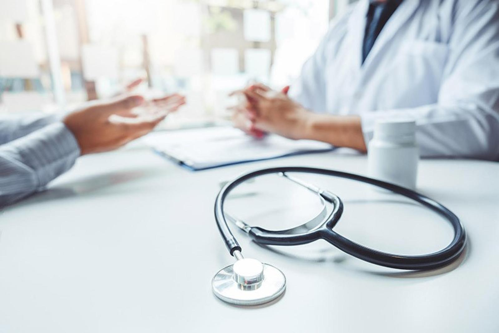 Doctor and patient in consultation discussing medical care at desk with stethoscope