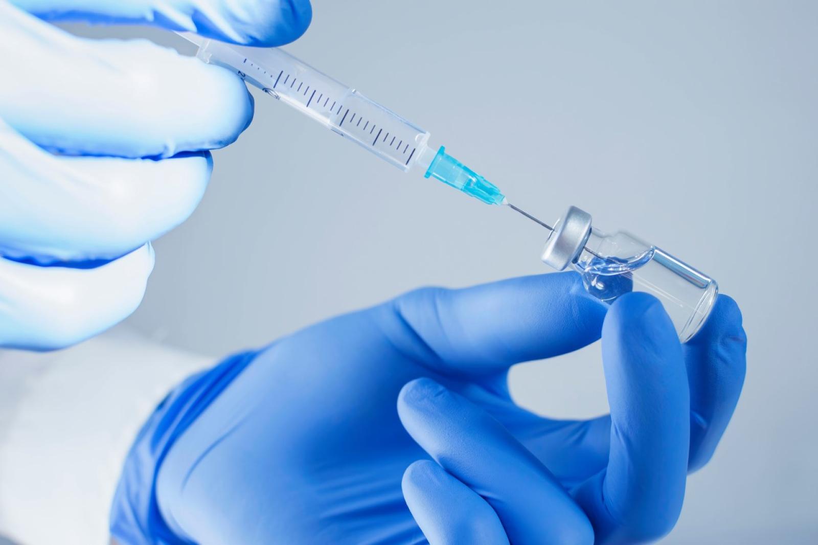 Healthcare professional in blue gloves preparing vaccine injection from vial using syringe